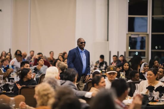 Abdi standing among sitting crowd